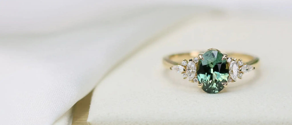 A delicate gold ring featuring a central oval-cut green gemstone flanked by smaller pear-shaped clear stones.