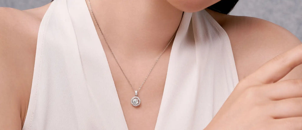 A delicate silver necklace featuring a round pendant with a central diamond surrounded by smaller diamonds in a halo design.